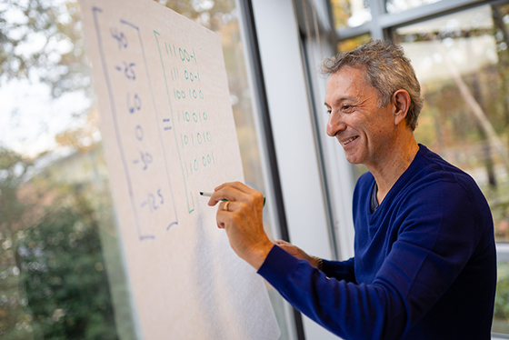 Jim Baldo is wearing a blue sweatshirt and writing calculations on a board.